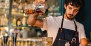 A barman pours a cocktail into a short glass