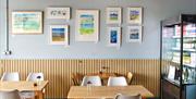 Inside the cafe, two tables set with a vase of flowers and paintings in the background.