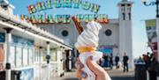 A hand holding an ice cream cone in front of the Brighton Palace Pier sign