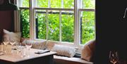 A seat by a window which shows a beautiful garden in the background.