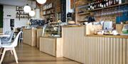 Tha main counter in the cafe with tables and white chairs in the foreground.