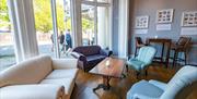 Comfy seating is laid out around a nice big table, next to a large window in the reception area of the hostel.