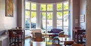 Comfy seating is laid out around a nice big table, next to a large window in the reception area of the hostel.