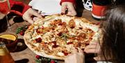 Diners at Franco Manca Brighton enjoying a tasty pizza. Image shows a close up of the pizza being shared by two people wearing red jumpers.