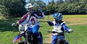 An adult and child on stationary motorbikes high fiving eachother.