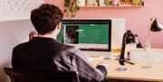 A person in a colourful workspace looking at a laptop, their back is to the camera.