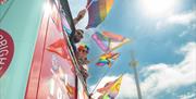 Pride attendees leaning over the side of a bus on the parade, waving Pride flags with a brilliant blue sky above them.