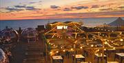 Image shows the Igloos at Brighton Music Hall, sparkling with fairy lights in front of a  beautiful Brighton sunset.