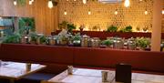 A view of the back wall of the restaurant, in the foreground traditional thali pots sit on a shelf in the dining area.