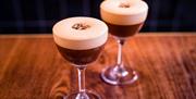Two espresso martinis on a wooden bar