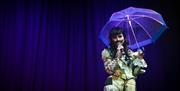 Image courtesy of dfphotography. Image shows a performer on stage in a suit, holding an umbrella