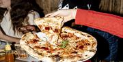 Diners at Franco Manca Brighton enjoying a tasty pizza. Image shows a close up of the pizza being shared by two people wearing red jumpers.