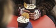 Two gloved hands holding cups of hot chocolate with cream.