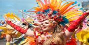 Image courtesy of JIm Carey. A Parade attendee wearing a wonderful, bright headdress with rainbow coloured feathers