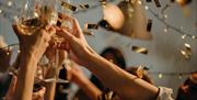Image shows guests celebrating at a Private Christmas party at DoubleTree by Hilton Brighton Metropole. Champagne flutes are raised in the air whilst