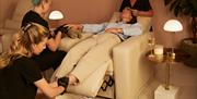A woman lies back whilst several beauty therapists work on her.