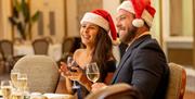 People in santa hats and drinking wine.
