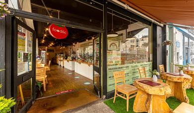Outside of the restaurant, a Foodilic sign hangs in a doorway with real wooden furniture outside