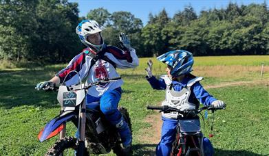 An adult and child on stationary motorbikes high fiving eachother.