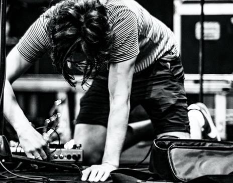 Black and white image of a person plugging in a pedalboard on stage