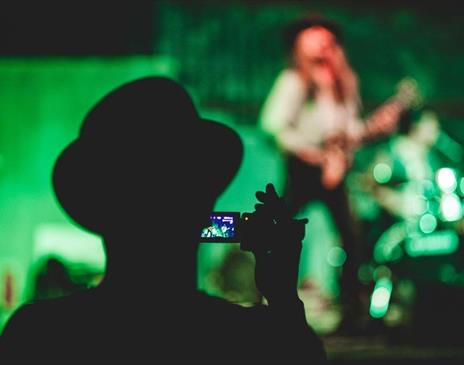 Person recording video of a person playing guitar onstage