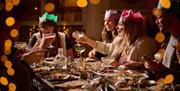 Partygoers enjoying a meal at Mowgli Brighton. a group of friends wearing colourful Christmas hats raise a toast, there are dishes of food in front of