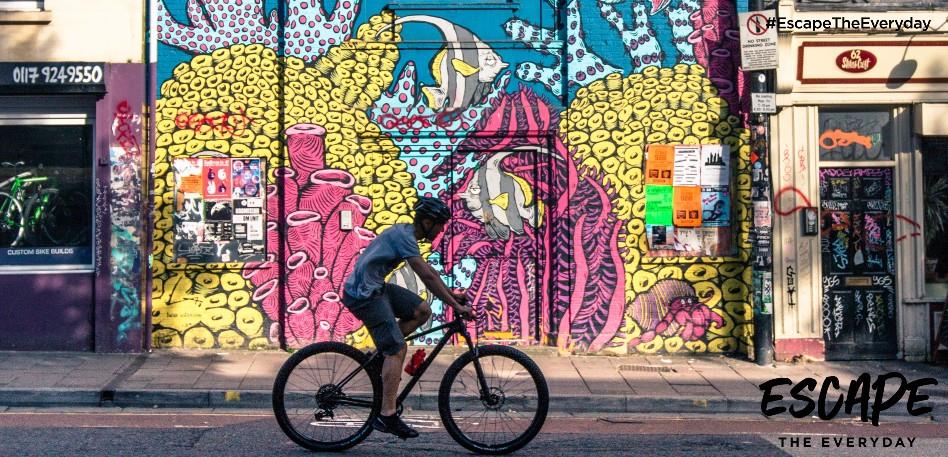 A person riding a bicycle past street art in Stokes Croft in Bristol
