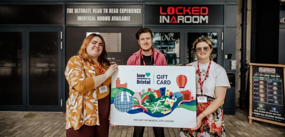 Locked In A Room in Bristol holding up a LoveBristol Gift Card outside their escape room