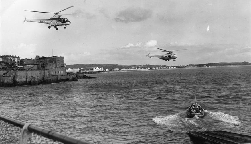 A black and white photo of two helicopters and a boat in the water