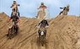 A group of five motorbike riders coming down a large sand dune