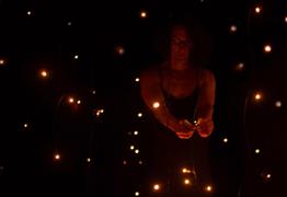 A lady in a dark room surrounded by fairy lights
