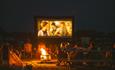 People watching outdoor cinema at night around bonfire