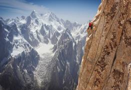 A climber scaling a cliff face against a backdrop of snowy mountains