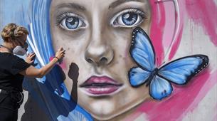 Person spraying mural of girl's face with butterfly