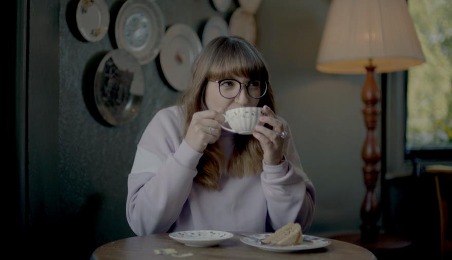 A women sat drinking a cup of tea and eating a slice of cake