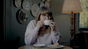 A women sat drinking a cup of tea and eating a slice of cake 