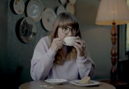 A women sat drinking a cup of tea and eating a slice of cake
