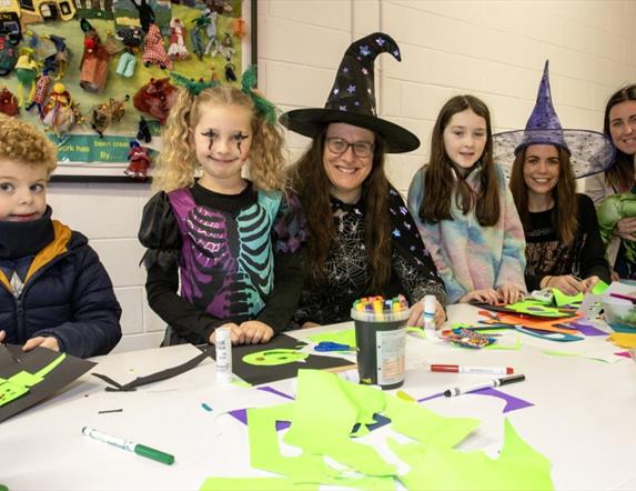 Image of children and faciltators in halloween fancy dress costumes crafting.