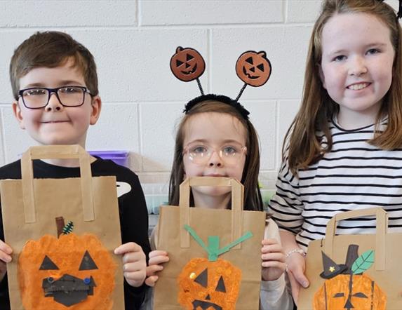 Imae of 3 children holding up their hand decorated pumpkin trick of treat bags.
