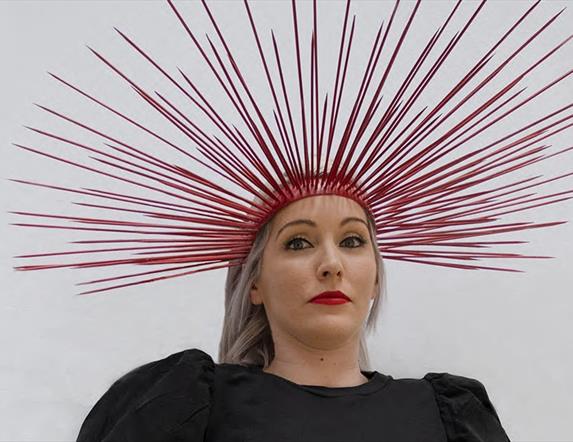 Image of a women in a black dress with a red flower in the middle and a red spiked headpiece
