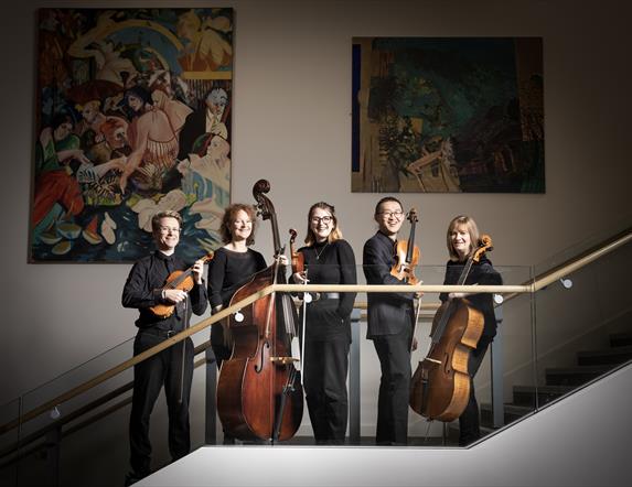 A group of orchestral musicians holding their instruments and standing in a line on a staircase.