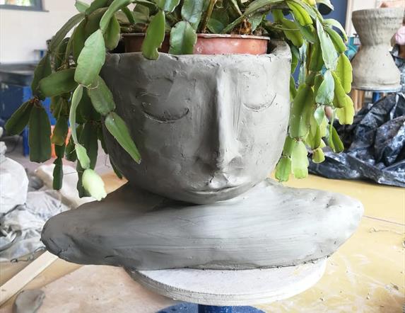 A ceramic planter made to look like a resting face, with a plant of hanging green leaves that resemble it's hair.