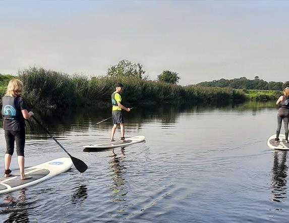a group of people using stand up paddleboards on the River Roe