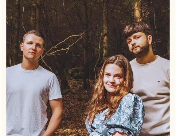 Image of 3 people standing outdoors looking at the camera, there is a forest in the background