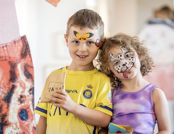 Two children with painted faces smile at the camera.