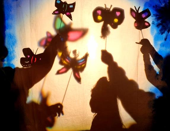 A number of small children cast colourful shadows across a wall using their puppets.