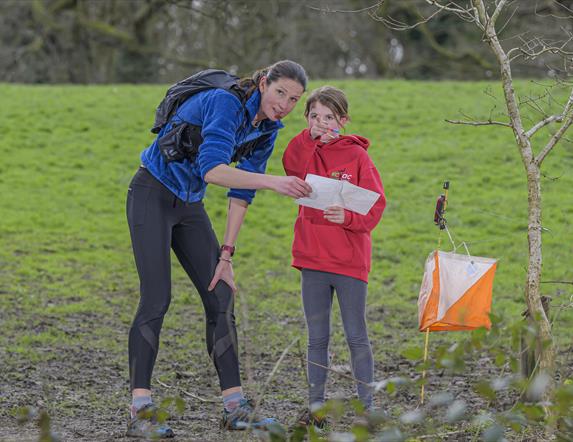 a woman and a girl outdoors, reading from a map. the girl is pointing the way