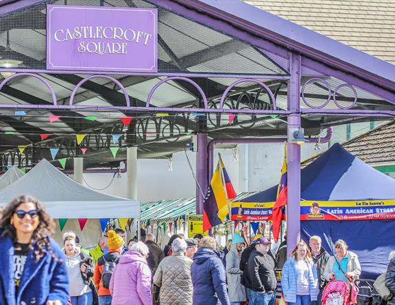 people walking through a market square with stalls