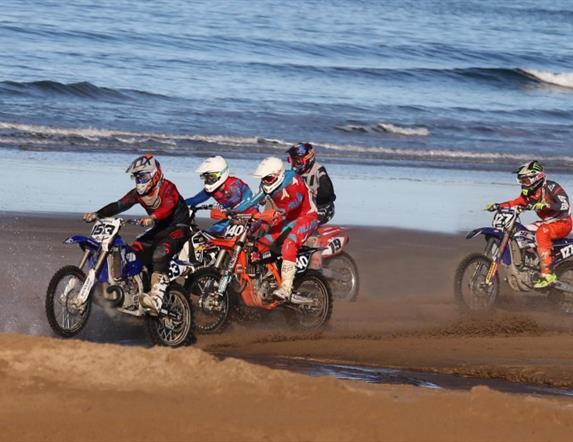 Riders on the sand with waves in the background