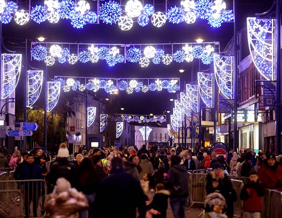 Image shows Christmas lights shining above a busy street with people shopping